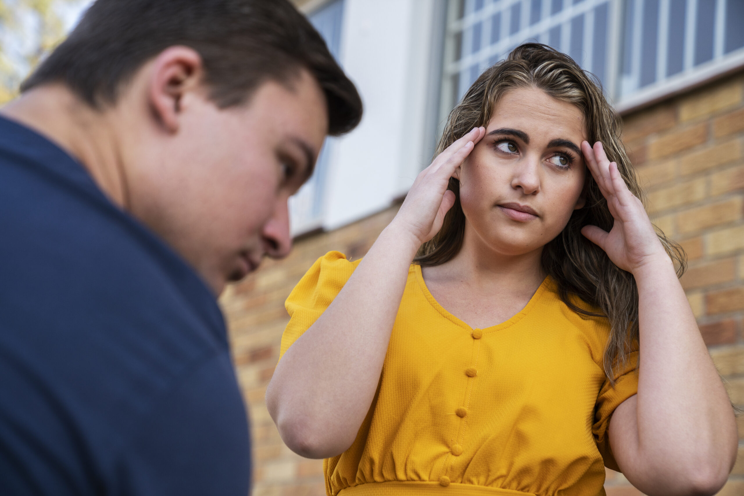 Duas pessoas, uma com a mão na cabeça de blusa amarela